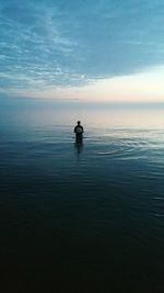 Silhouette men in sea against sky during sunset