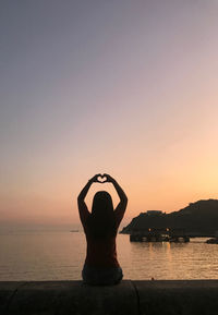 Silhouette woman making heart shape against sky during sunset