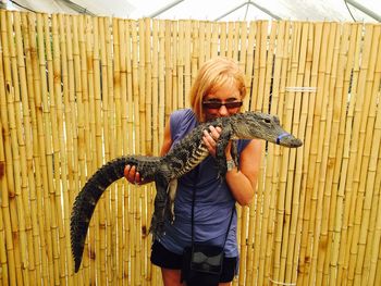 Woman holding alligator against fence