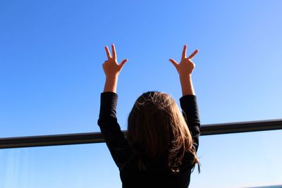 Rear view of girl gesturing against clear blue sky