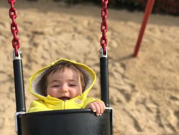 Cute baby wearing yellow warm clothing on swing at playground