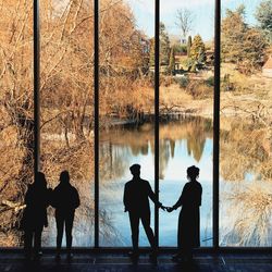 Rear view of silhouette people standing on footbridge by lake during winter