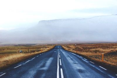 Road leading towards mountains against sky