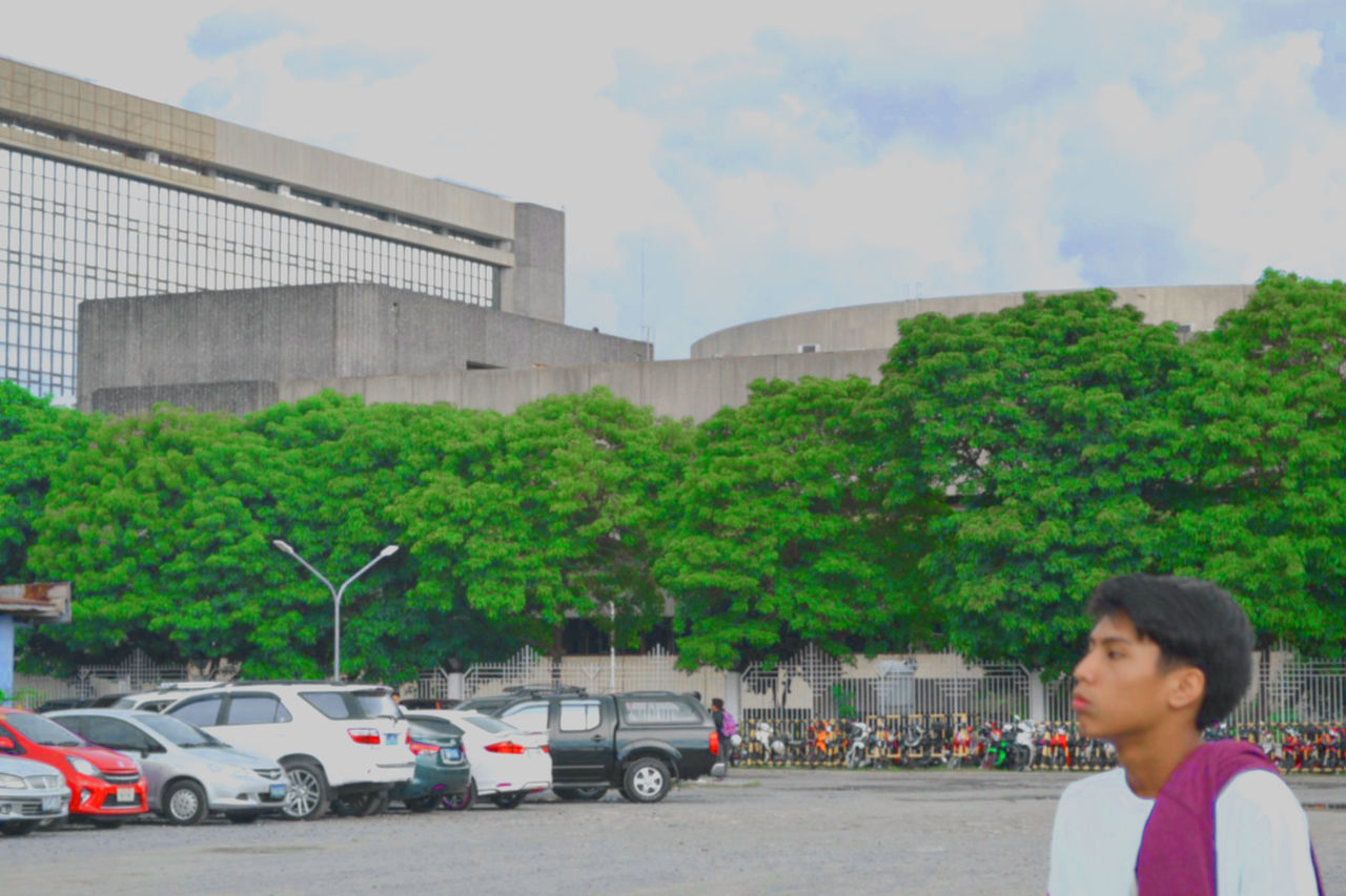 transportation, mode of transport, architecture, land vehicle, built structure, tree, building exterior, side view, casual clothing, young women, person, young adult, cloud - sky, green color, outdoors, day, sky, in front of, city life