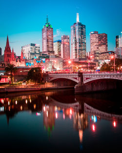 Illuminated buildings by river against sky in city at night