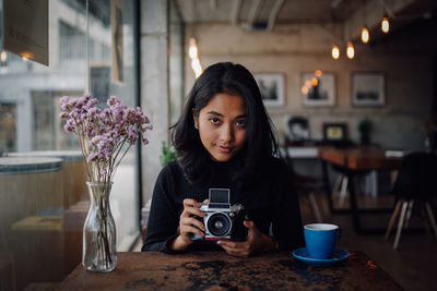 Portrait of woman photographing with camera at table in cafe