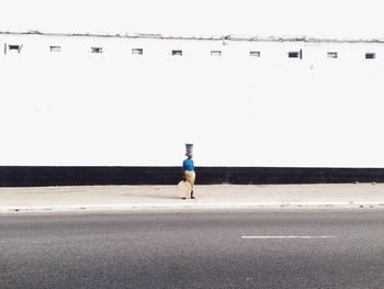 Woman standing on road by building against clear sky