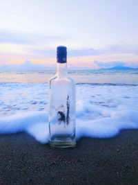 Drinking glass on beach against sky during sunset