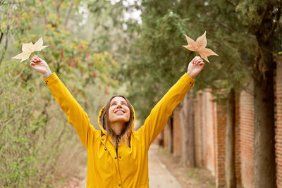 Rear view of woman with arms raised standing against trees