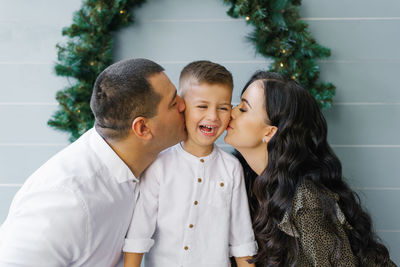 Beautiful young mom and dad kiss a cute little son standing against 