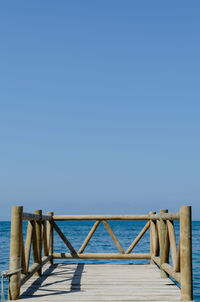 Pier over sea against clear blue sky