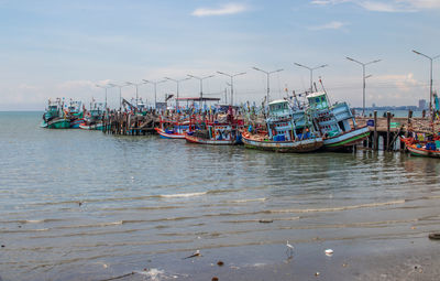 Fishing boats moored at harbor against sky