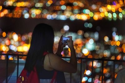 Woman photographing illuminated city through smart phone at night