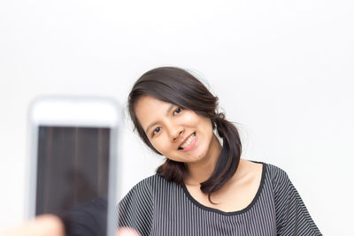 Portrait of smiling young woman using smart phone against white background