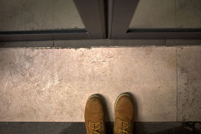 Low section of man wearing shoes standing by closed door