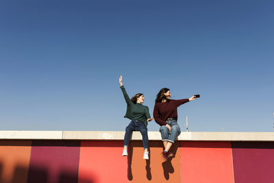 Carefree female friends taking selfie while sitting on retaining wall