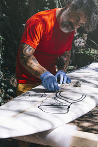 Surfer man cleaning surfboard from old wax. person