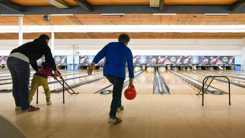 Older woman and father with child bowling together at bowling alley.