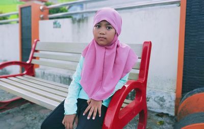 Portrait of girl sitting against pink wall