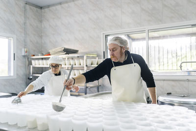 Skilled chef couple making cheese in containers at factory