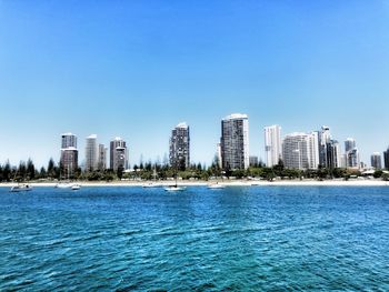 City skyline by sea against clear blue sky