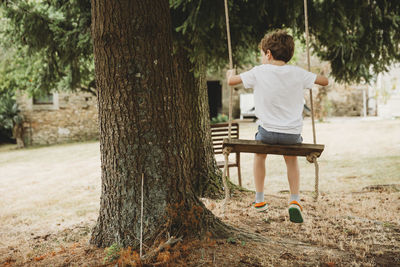 Rear view of boy on swing under trees