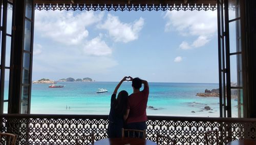Rear view of couple making heart shape at beach against sky