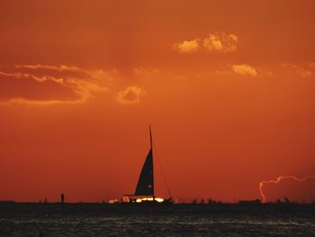 Silhouette sailboat sailing on sea against orange sky