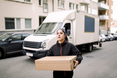 Young delivery woman carrying package while walking on street in city