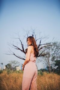 Portrait of young woman standing on grassy land against clear sky