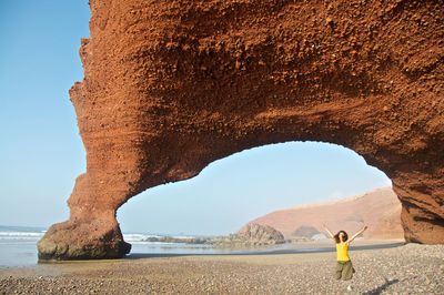 Woman jumping on beach against rock formation