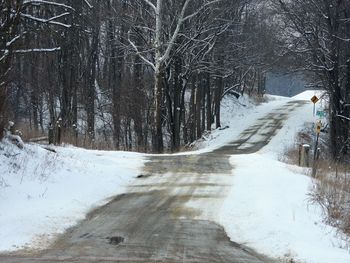 Snow covered road amidst trees during winter