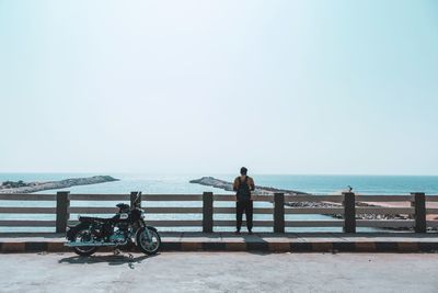 Man on retaining wall by sea against clear sky