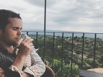 Young man drinking by railing against sky