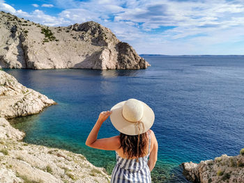 Woman standing on rocky shore, admiring the view, sea, summer, one person, hat.