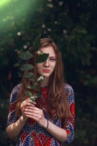 Portrait of young woman covering eyes with leaf