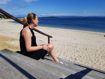 Woman looking away while sitting on staircase at beach