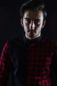 Portrait of handsome serious young man against black background