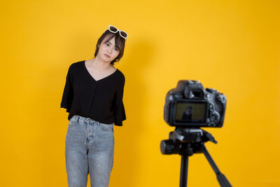 Vlogger making video while standing against yellow background