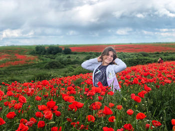 Portrait of young woman with red poppy flowers in field