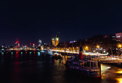 Illuminated city by river against sky at night