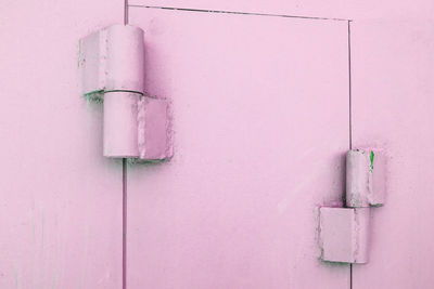 Close-up of metal hinges on the gates of a metal garage, painted pink, outdoors.