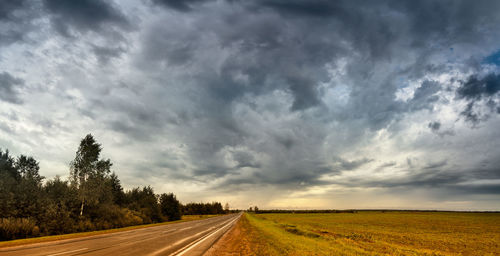 Road passing through field against storm clouds