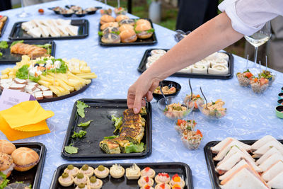 Cropped hand of woman taking food from tray on table