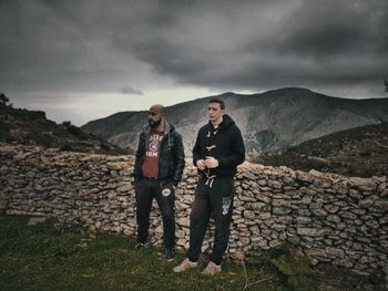 Full length of friends standing on rock against sky