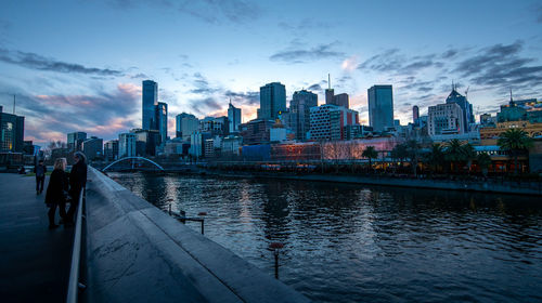 River amidst buildings in city against sky at dusk