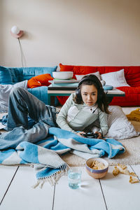 Young woman playing video game while lying in living room at home