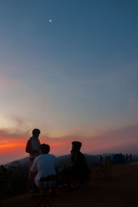 Silhouette people sitting on land against sky during sunset