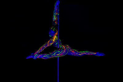 Full length of woman wearing neon clothing doing pole dance against black background