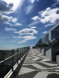 Empty footpath by buildings against sky on sunny day